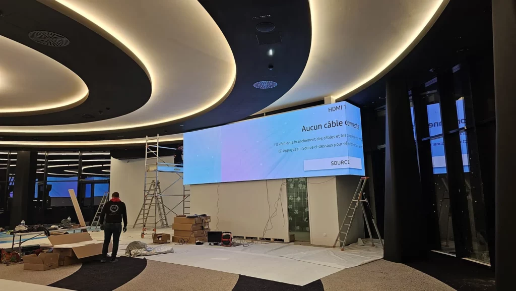 Écran LED d'angle en cours d'installation sous un plafond lumineux, techniciens sur échafaudage