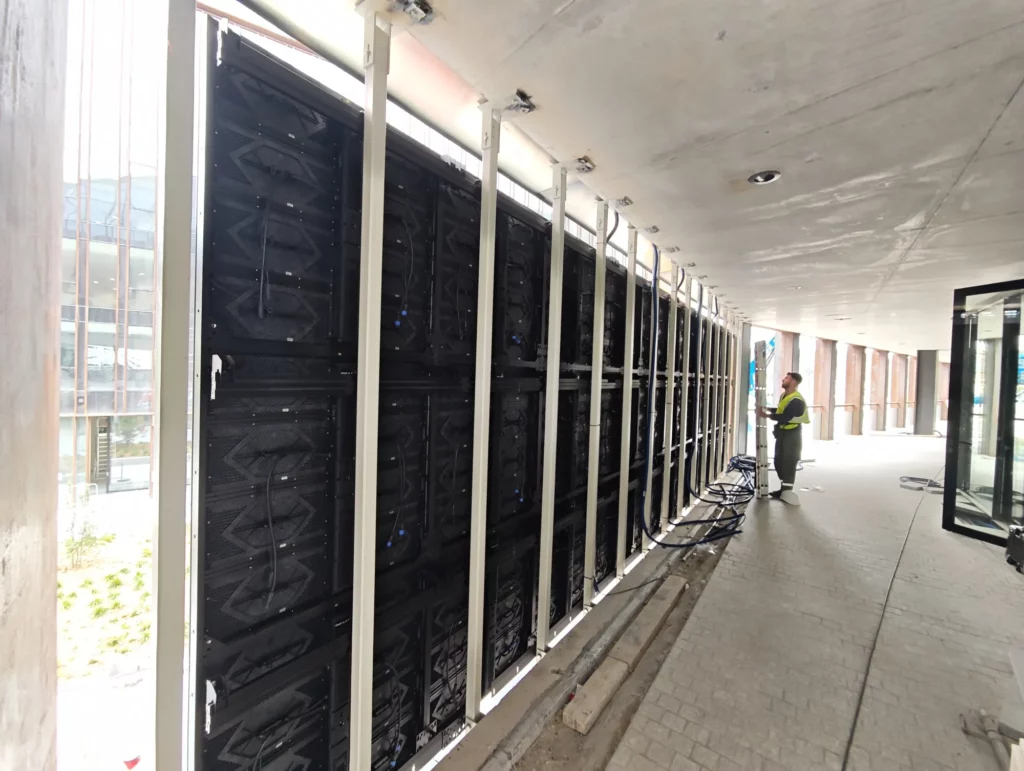 Structure arrière et câblage d'un écran LED de façade, avec un technicien debout à droite